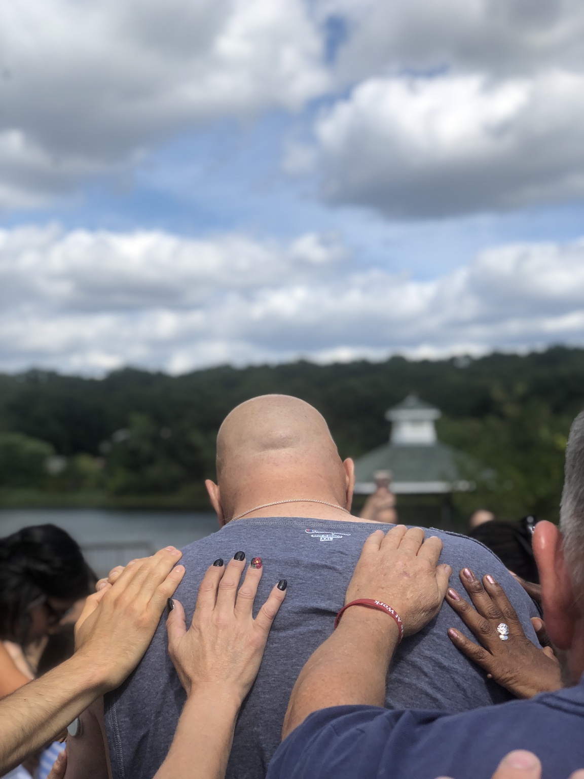 People rest their hands on a man’s shoulders as they pray together beside the water