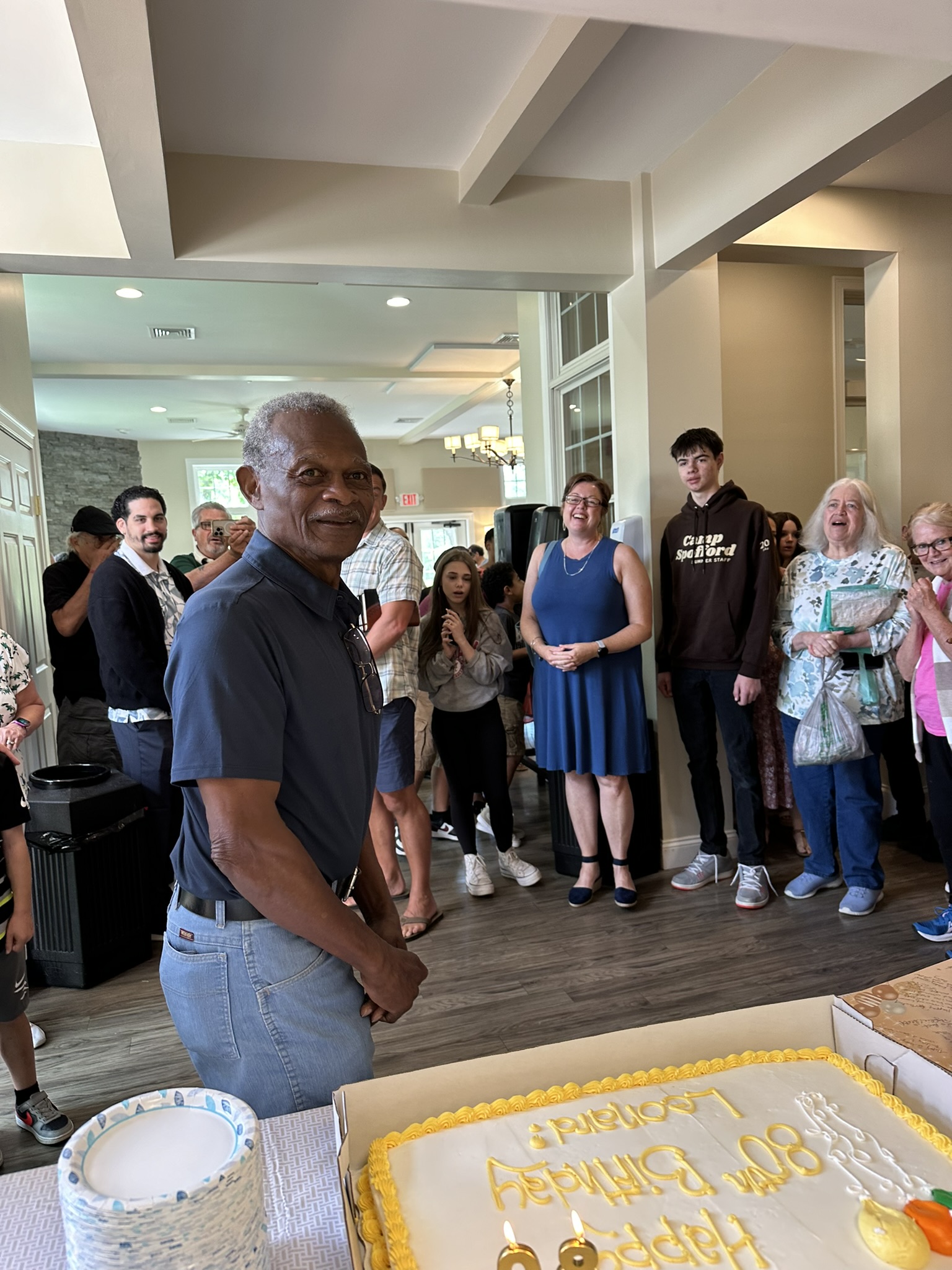 A birthday celebration at Living Faith, with the guest of honor beside his cake and church friends of different generations gathered around him